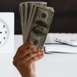person holding money in front of a clock