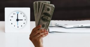 person holding money in front of a clock