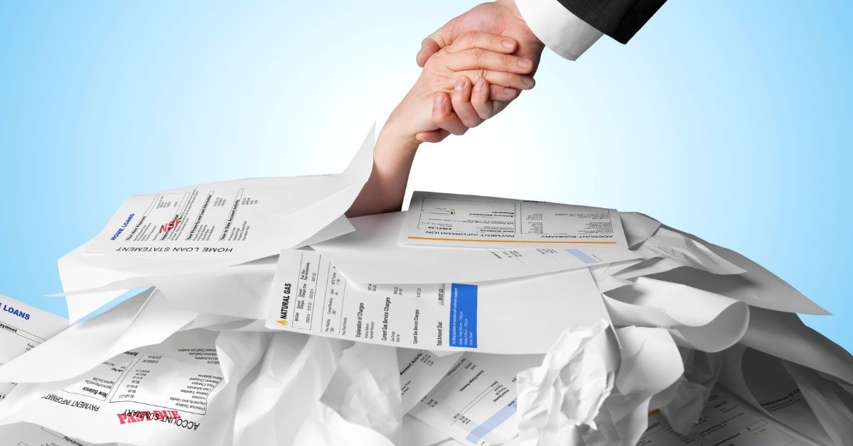 person giving a helping hand to someone in debt under pile of past due bills