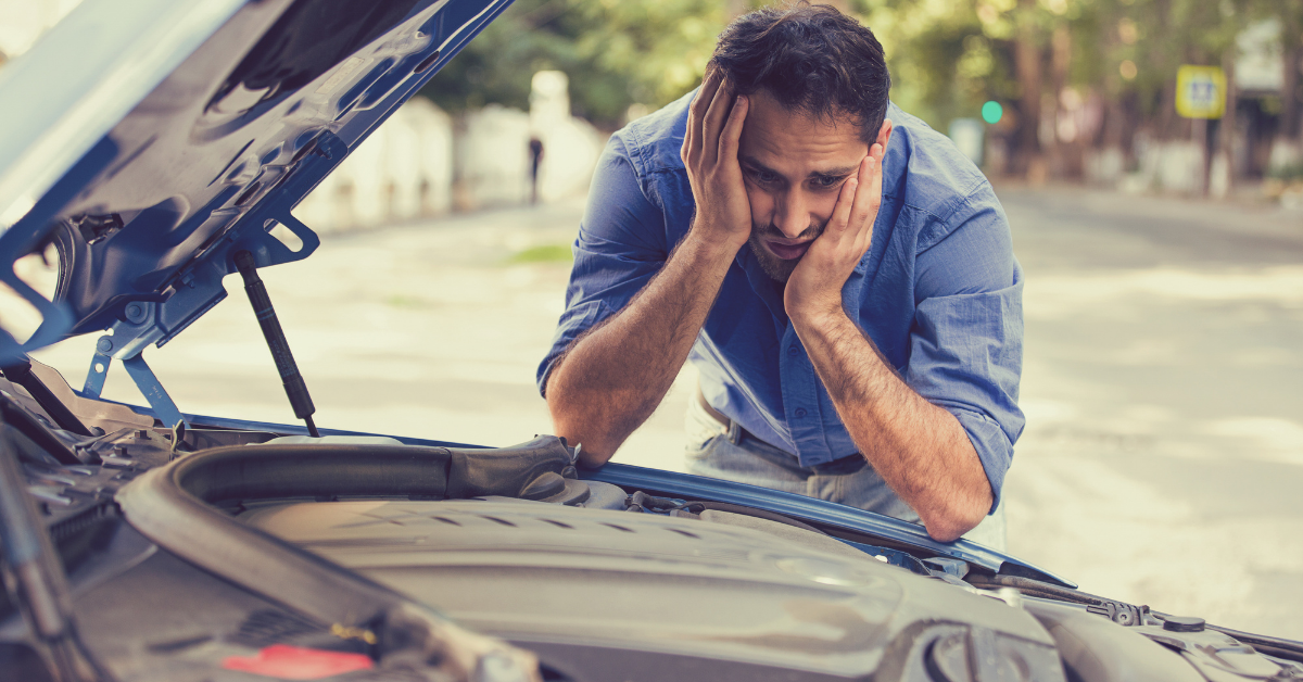 man looking under hood of his car that broke down