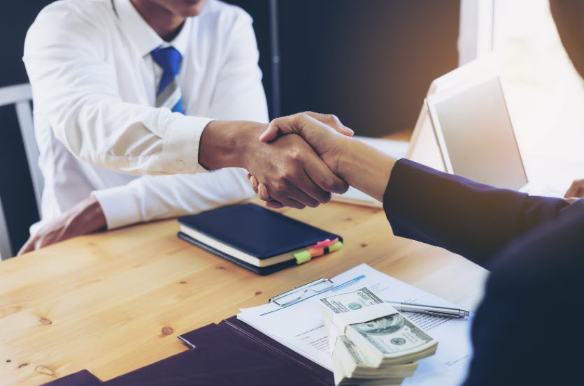 Two people are shaking hands across a table. One is in a button down shirt, the other is in a suit jacket, implying that they just agreed on something business related. This article discusses cash loans.