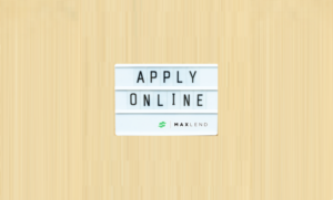 A white sign that says "APPLY ONLINE" in capital letters and has the MaxLend logo on the bottom corner of is on top of a beige-colored background. This indicates that the blog is about Applying for a Loan With MaxLend.