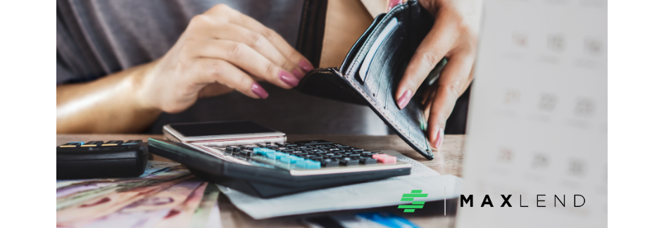 A person with pink painted fingernails is looking inside an empty wallet while a calculator lies in front of her. This implies she is struggling with money.