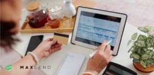 A person reviewing bills on a tablet while holding a credit card, with a notebook and calculator nearby, symbolizing financial planning and loan options for paying bills.