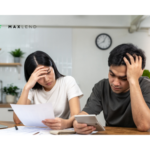 A couple sitting at a table with paperwork and a calculator, looking stressed while discussing their finances, symbolizing the challenges of talking about loans together.