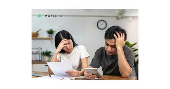 A couple sitting at a table with paperwork and a calculator, looking stressed while discussing their finances, symbolizing the challenges of talking about loans together.