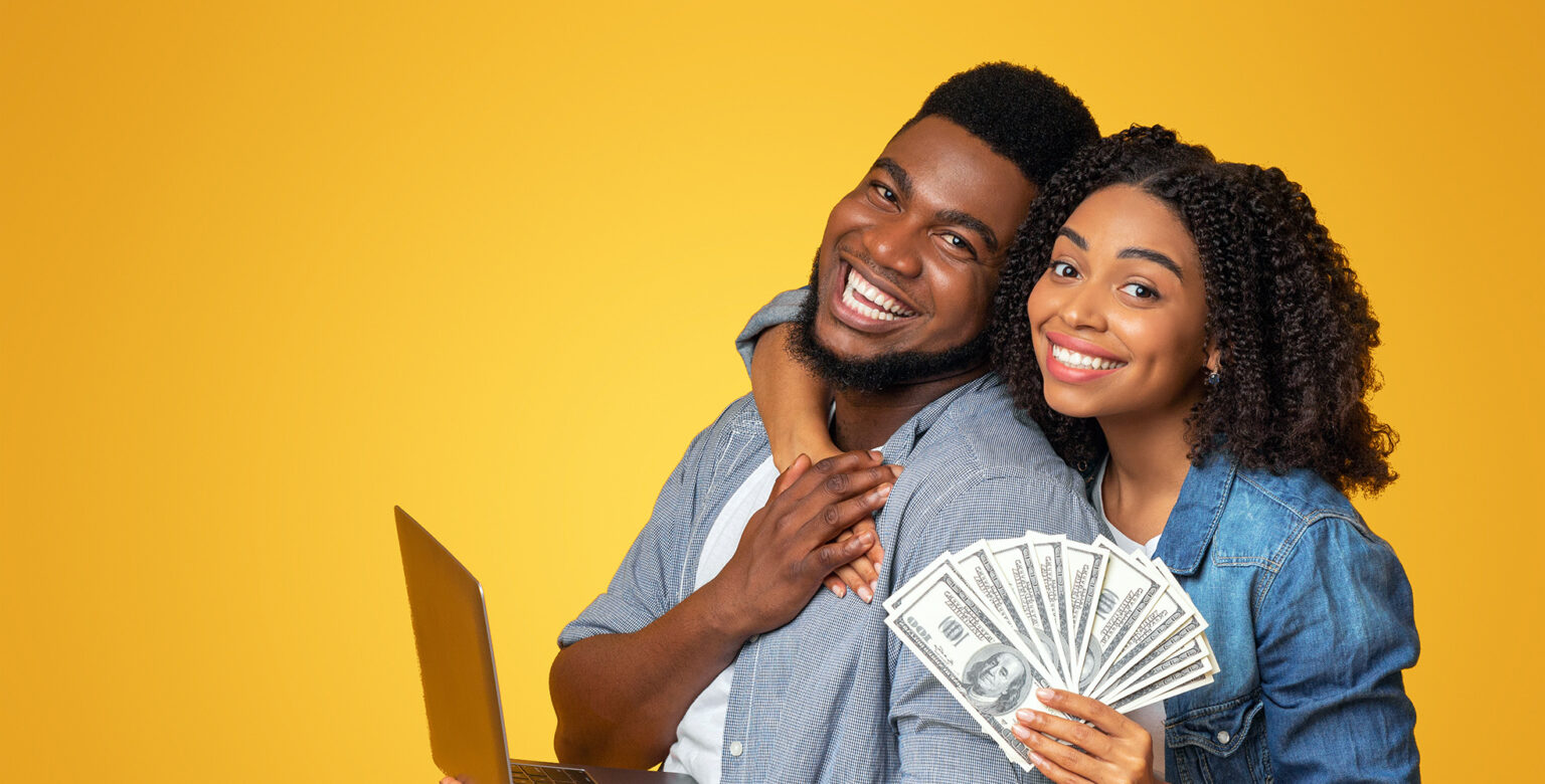 A man and woman are standing together, smiling, hands touching. He is holding a laptop computer and she is holding cash.